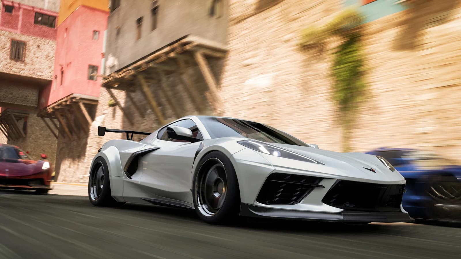 A white Chevrolet Corvette races alongside other cars on a paved street between buildings in Forza Horizon 5.