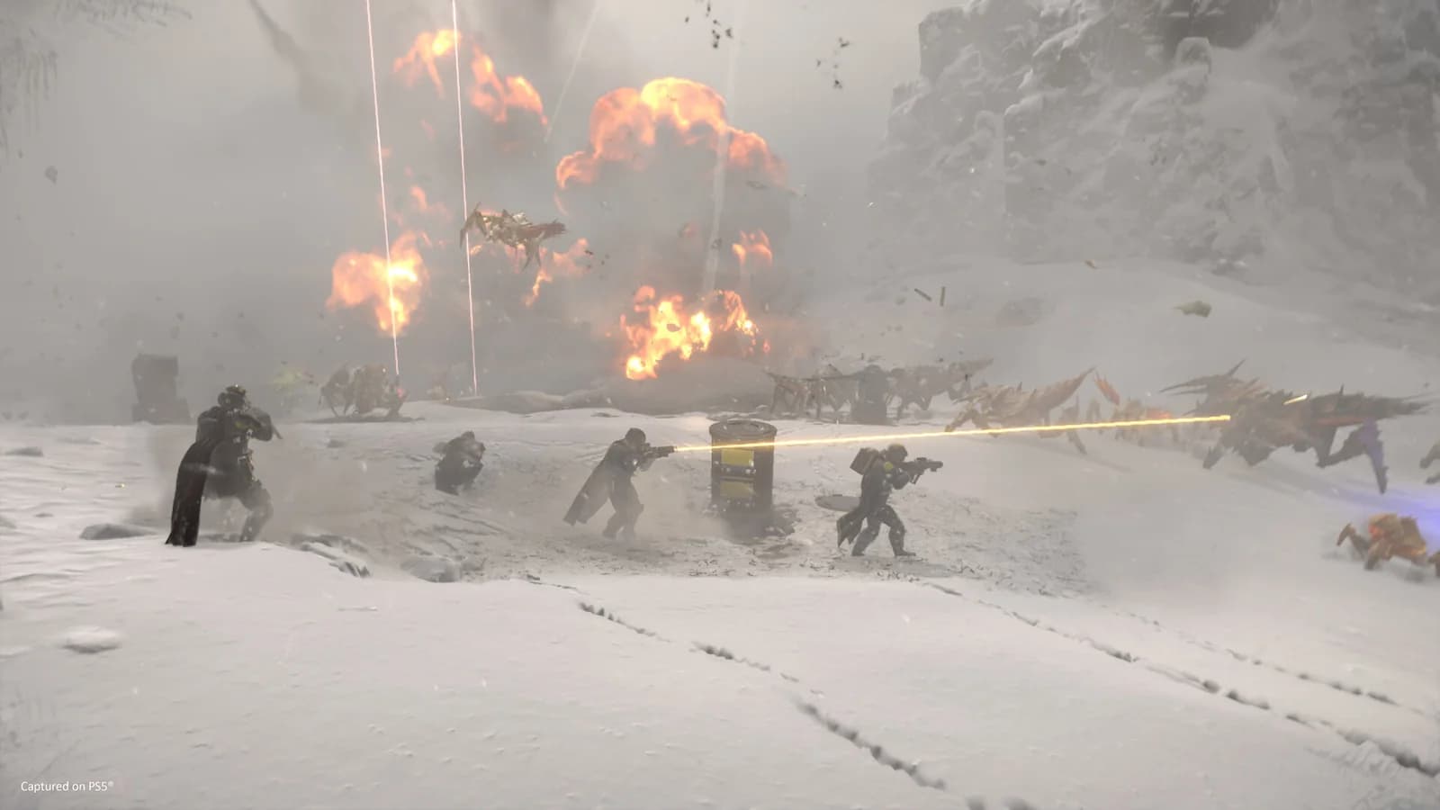 Four Helldivers spread across a snowy battlefield, firing toward insect-like enemies while explosions rise behind them.
