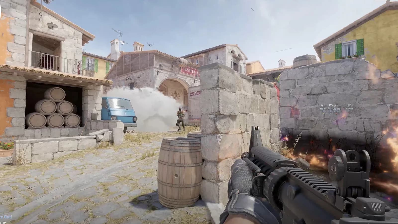 A first-person Counter-Strike 2 view beside stone cover, with smoke near a blue van and teammate outlines visible behind a wall.